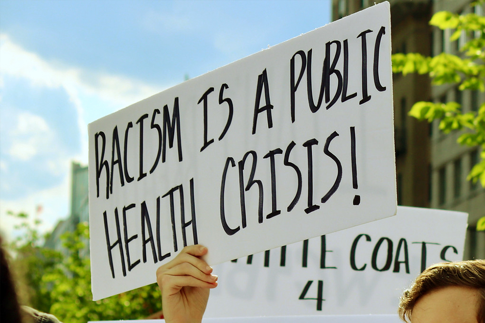 Person holding a sign reading racism is a public health crisis