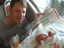 2015-16 Management Certificate program scholar John Thompson holding his baby's newborn screening paperwork.