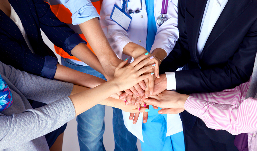 Photograph of a circle of people clasping hands in the middle of the group.