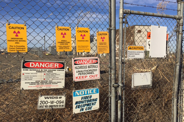 Photograph of a chain link fence with many warning signs posted on it.