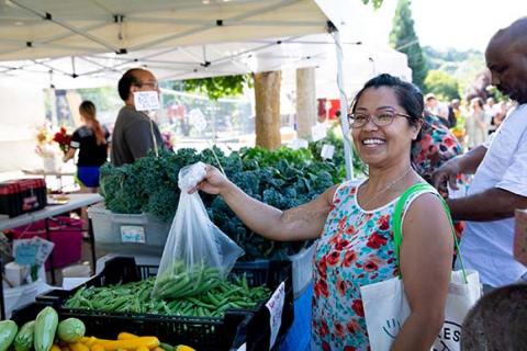 Photograph of a woman holding a bag of produce at a farmers market stall.