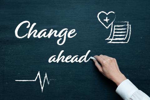 Graphic of a person's hand writing the phrase Change Ahead on a blackboard.