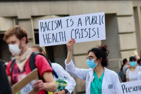 woman holding "racism is a public health crisis" sign