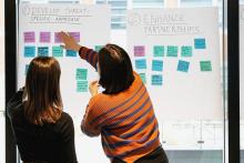 Photograph of coordinating body members pointing to post-its on a large white paper during a brainstorming activity