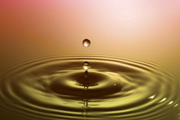 Photograph of a water droplet splashing with an expanding wave around it.