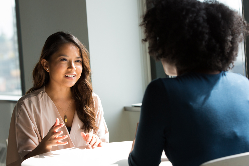 Photograph of two people talking over a table.