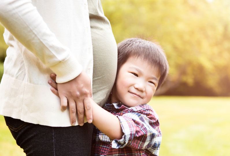 Photograph of a young child hugging a women's pregnant stomach.